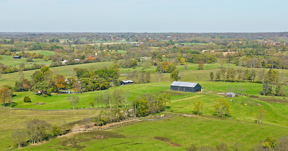 Aerial still of barn and farmhouse near Georgetown, a city in Scott County, Kentucky, on a mostly clear day in Fall.