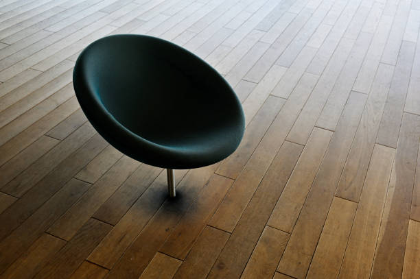 A lone black chair stands stoically on the polished wood floor, a striking contrast against the warm tones of the indoor space