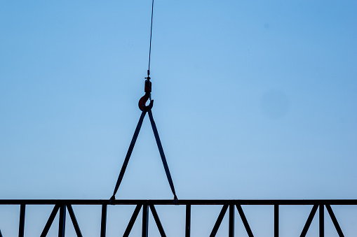 A piece of steel construction carried by a crane. Silhouette shot with copy space.  Perfect for roofing, construction, and industry themes.