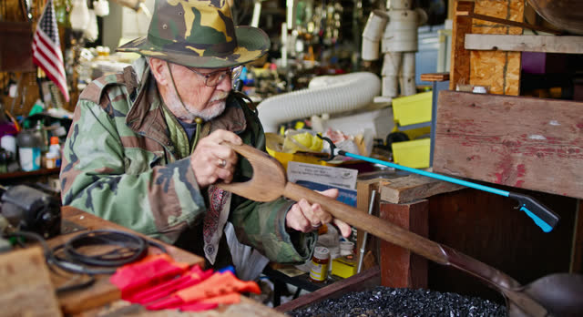 Elderly Veteran Keymaker Shoveling Coal inside Workshop