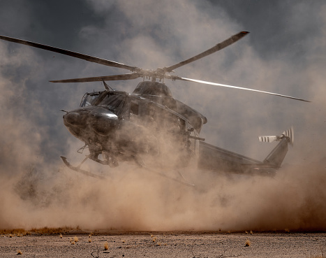 A Bell 412 military helicopter lands in the desert with soldiers