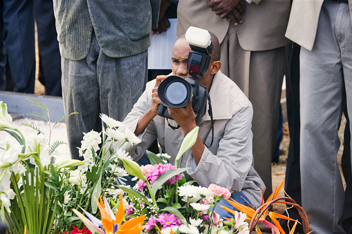 young african photographer taking pictures at a funeral over the flower on the grave