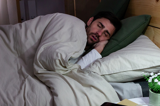 young man sleeping in bed at home in the early morning, insomnia