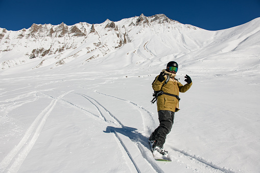 active male snowboarder riding freeride on powder snow down the slope against the backdrop of the mountains