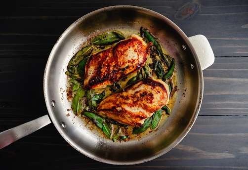 Marinated chicken breasts and fresh sage leaves frying in a large pan