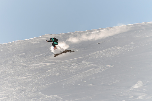 Great view on active male freerider on snowboard speedly descends an off-piste on fresh snow of mountain hill