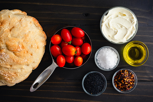 Crusty French bread, grape tomatoes, mascarpone cheese, and other ingredients on a rustic wood table
