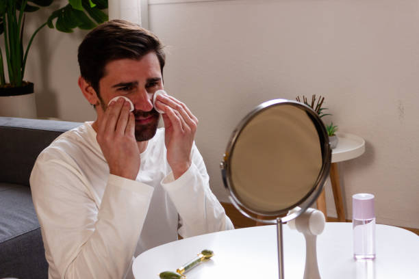 istock Young man applying face cream in front of a mirror at home. 1895692037