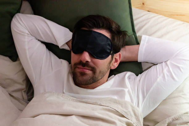 istock Young man sleeping in bed with blindfold on his eyes, top view 1895696675
