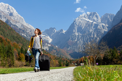 Handsome Tourist Mid Adult Woman Walking with a Big Rolling Suitcase Trough a Beautiful Alpine Mountains Valley