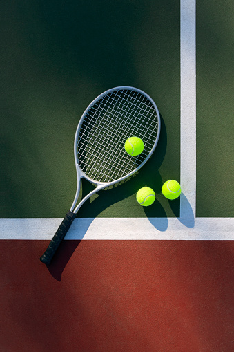 Tennis racket and three balls on an outdoor tennis court