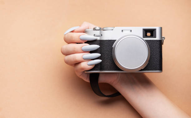 istock Woman's hand with grey nail polish holding camera 1895929376