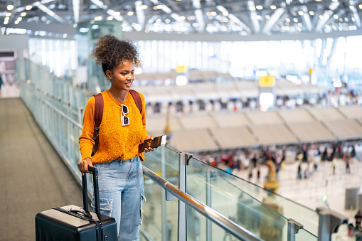 African woman with suitcase walking to check-in counter at airport terminal and waiting flight boarding airport departure hall. Attractive girl enjoy travel on holiday vacation with air transportation