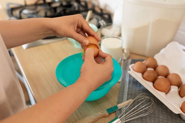 istock a woman breaks chicken eggs in a bowl while standing in the kitchen 1895946136