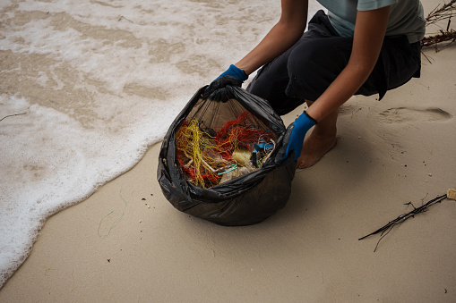 A close-up shot of a volunteer's hand holding the garbage bag on the beach.