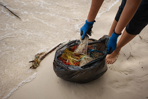 A close-up shot of a volunteer's hand picking up plastic on the beach.