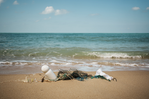 A small piece of plastic, discarded, nylon fishing net, on a sandy beach, posing a threat to wildlife.
