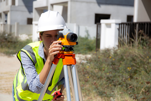 Surveyor woman using theodolite at construction site, engineer survey measuring land and examining road, one person, industrial concept.