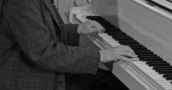 A man playing the piano.  Black and white photograph.   View from shoulders down.  Unrecognizable person.
