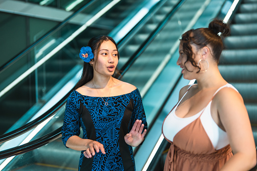 Two Pacific Islander women standing on escalator conversating with each other.