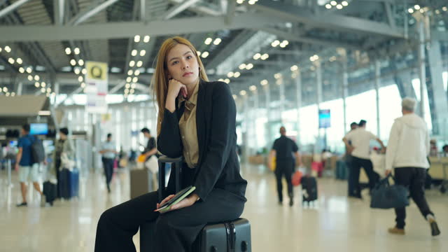 4K Asian businesswoman waiting for flight boarding at airport terminal.
