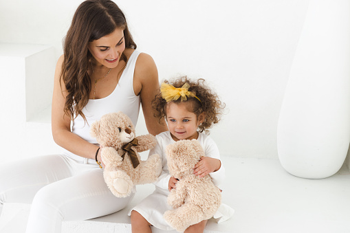 Portrait of a beautiful young mother with long hair, embracing her toddler daughter in the living room