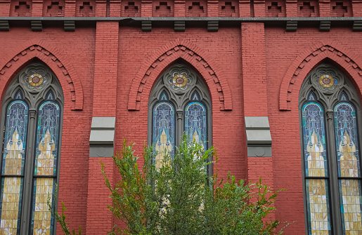 The side of a historic church building with red brick and stained glass windows