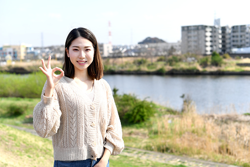 Young Asian woman in casual clothes giving an OK sign outdoors