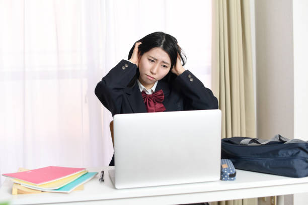 istock A young Asian female student is sitting at her desk and thinking while holding her head. 1896605047