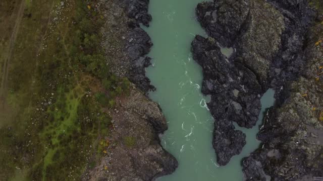 Drone view of flowing river water through rocky stones under bridge in daylight