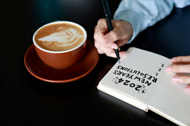 istock Young female writing her 2024 New Year's Resolutions on a notebook, coffee cup on desk 1896699121