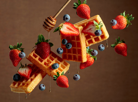 Waffles with blueberries and strawberries are watered with honey. Food levitation. Copy space.