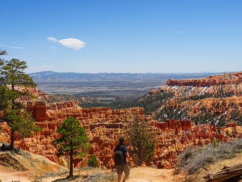 Bryce Canyon, Utah, USA. April 30th 2023. A man walking towards a look-out point in Bryce Canyon, on a warm and bright spring day. Blue sky and snow on the higher grounds. Orange rocks and hoodoos.