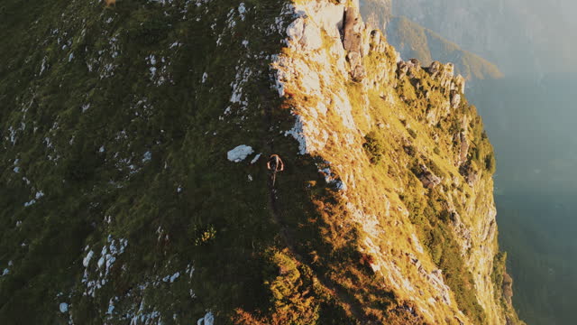 Aerial Drone Footage of Determined Male Mountain Biker Cycling on Rocky Cliff during Sunny Day