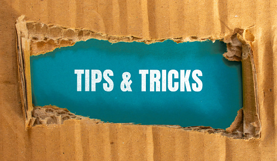 Tips and tricks lettering on ripped cardboard paper with blue background. Conceptual photo.