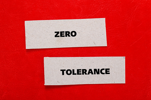 Zero tolerance lettering on ripped paper pieces with red background. Conceptual photo. Top view, copy space.