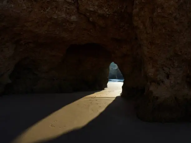 Photo of Luminous Portal: Sunbeam Illuminating a Coastal Cave Entrance, Creating a Path of Light in the Sand.