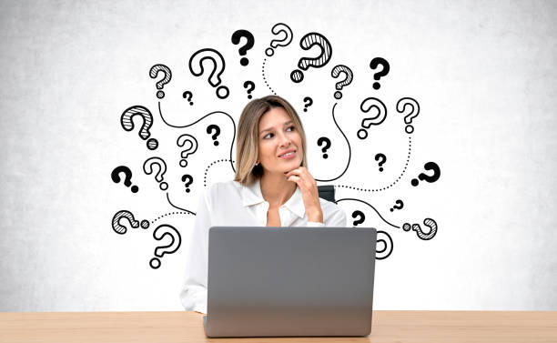 istock Pensive young woman with laptop, question marks on grey concrete wall 1896813321