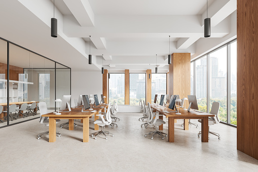 Interior of modern open space office with white walls, wooden columns, concrete floor and rows of wooden computer desks with chairs. 3d rendering