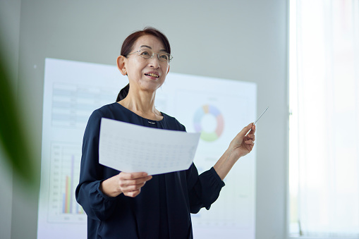 A senior Japanese woman giving a presentation at the office