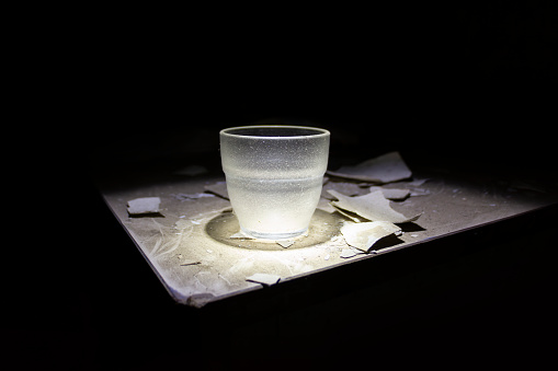 An old glass, illuminated by a light, placed on a dirty table in the dark