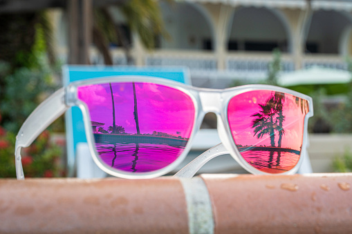 Clear sunglasses, with a tropical scene and palm trees, reflected in their pink, mirrored lenses