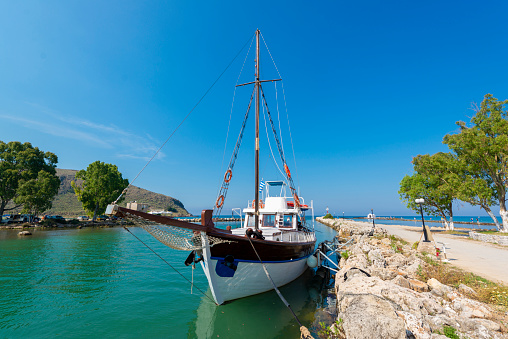 Beautiful travel image with entrance of the harbor Mandraki on Rhodes Island, Greece. Luxury yacht docked in port at the fortification. Famous deer statues at the entrance. Blue sky and clouds.