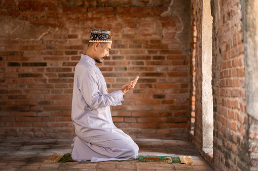 Muslim man praying for blessings in a sunlit old Islamic of mosque.