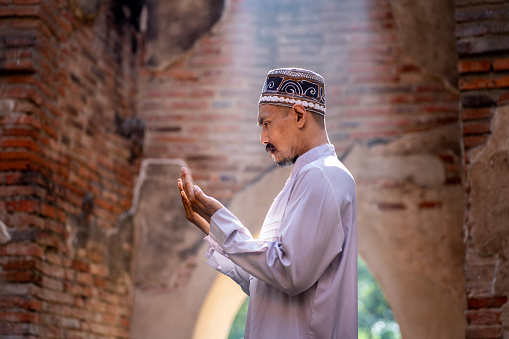 Muslim man praying for blessings in a sunlit old Islamic of mosque.