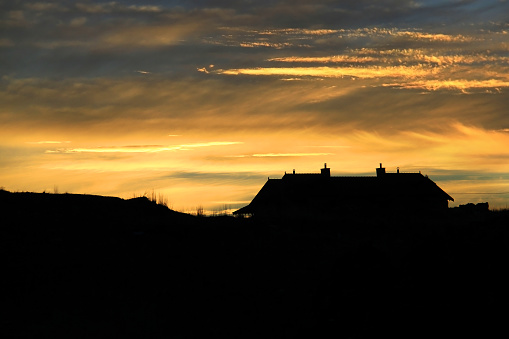 Silhouette of a house against a cloudy sky with the setting sun.