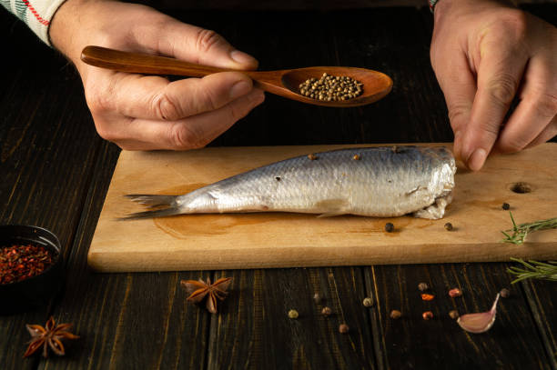 istock Cooking marinated fish Clupea with aromatic spices by the hands of a chef on a cutting board. Fish diet cooking concept on kitchen table 1897229949