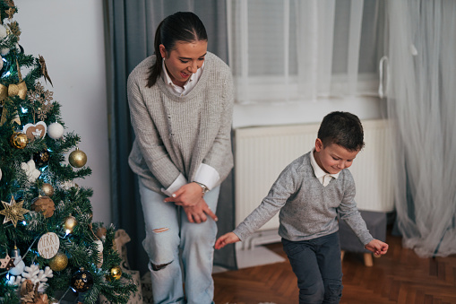 Happy mother with son dancing around glowing Christmas tree in living room