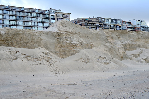 Blankenberge, West-Flanders, Belgium - December 29, 2023:  yearly maintenance draining beach sand. Sand hill heap in front of boardwalk and first line coastal apartments