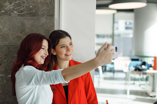 Workplace Connection: Young Employees Taking Selfies or Video Call in Modern Office. Experience the connectivity of the modern workplace with this engaging stock photo, featuring young employees taking selfies or making a video call in a contemporary office setting. The image captures the tech-savvy and collaborative nature of the workforce, where professionals seamlessly integrate moments of connection into their work routines. Ideal for portraying the dynamic and social aspects of the workplace, this photo is perfect for business-related promotions, teamwork publications, and social media content celebrating the vibrant interactions among colleagues. Workplace connection, Young employees, Taking selfies, Video call, Modern office, Businesswoman, Connectivity, Tech-savvy, Collaborative, Workforce, Business-related promotions, Teamwork publications, Social media content, Vibrant interactions